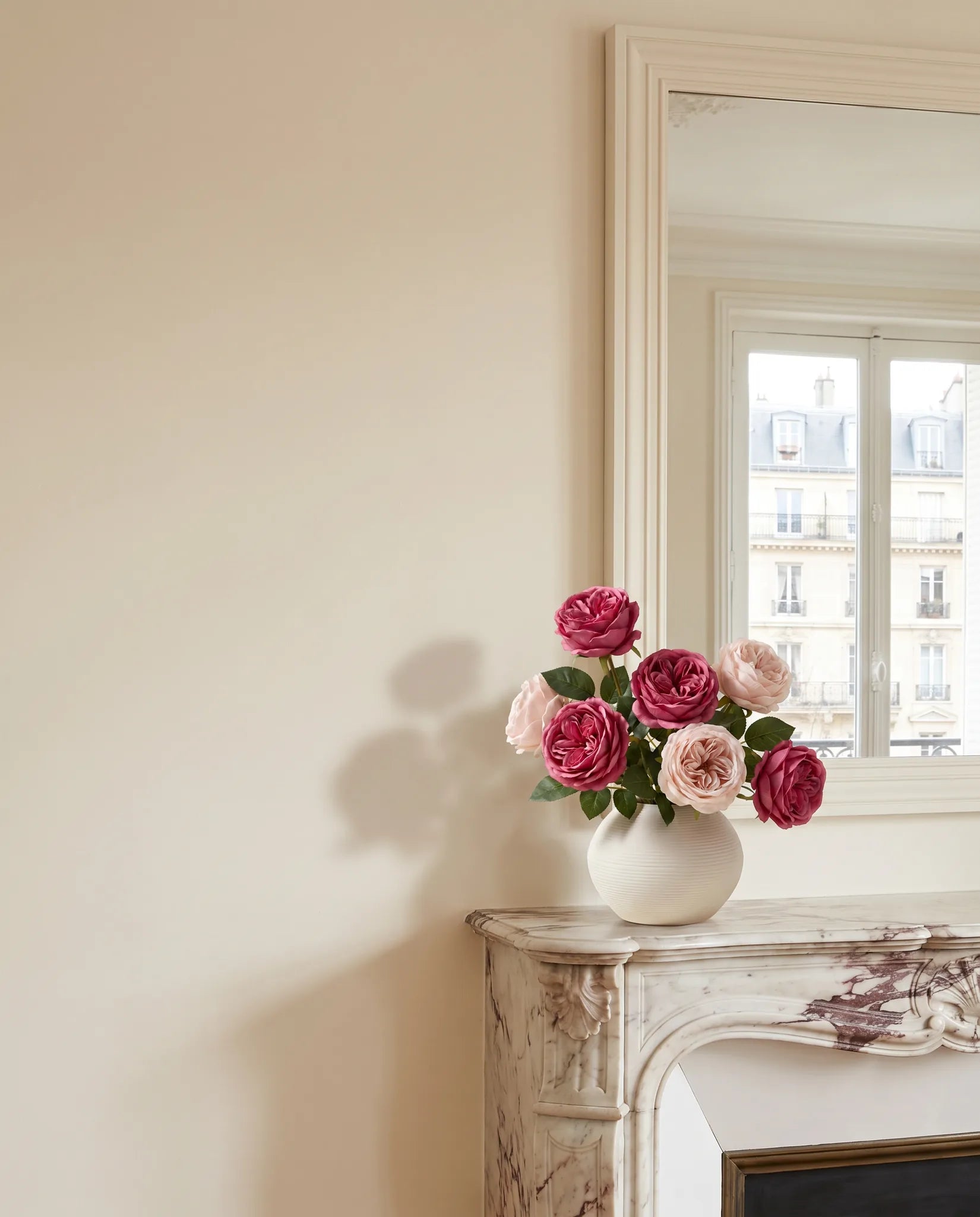 Bouquet artificiel rose magenta sur une cheminée en marbre, salon parisien rénové