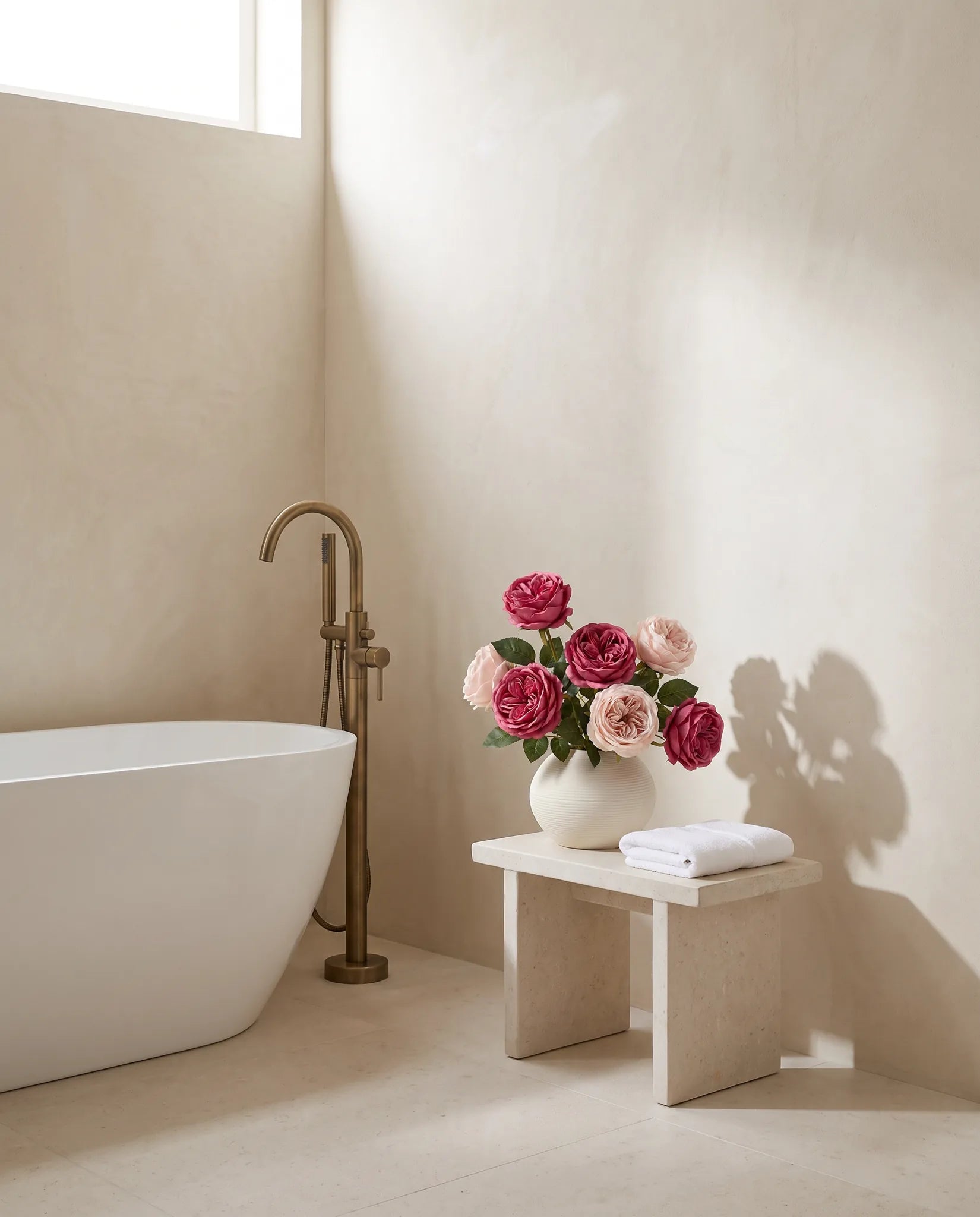 Bouquet artificiel rose magenta sur un tabouret en pierre près d'une baignoire îlot