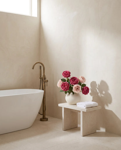 Bouquet artificiel rose magenta sur un tabouret en pierre près d'une baignoire îlot