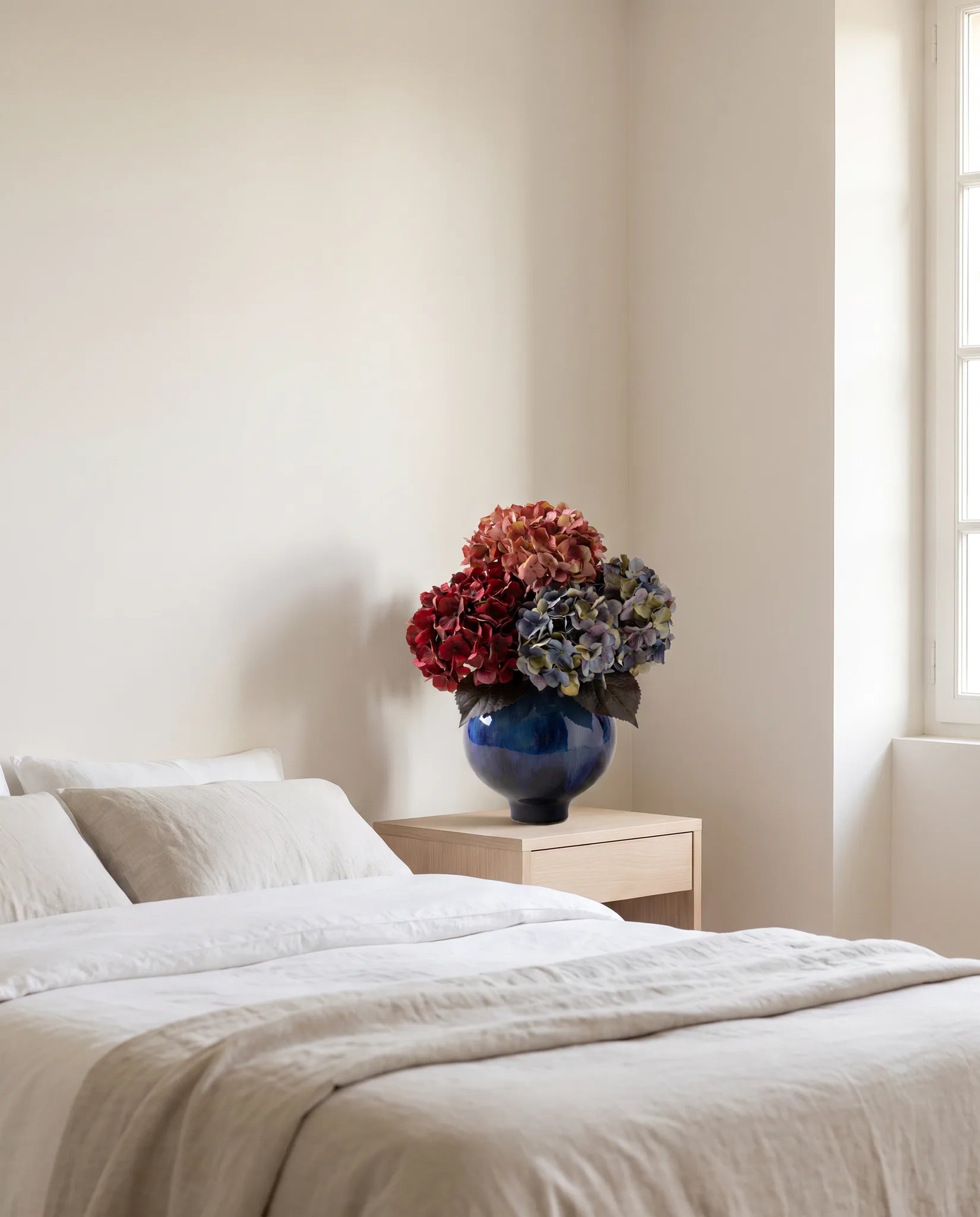 Bouquet artificiel rose et bleu sur une table de chevet en bois clair, chambre en lin