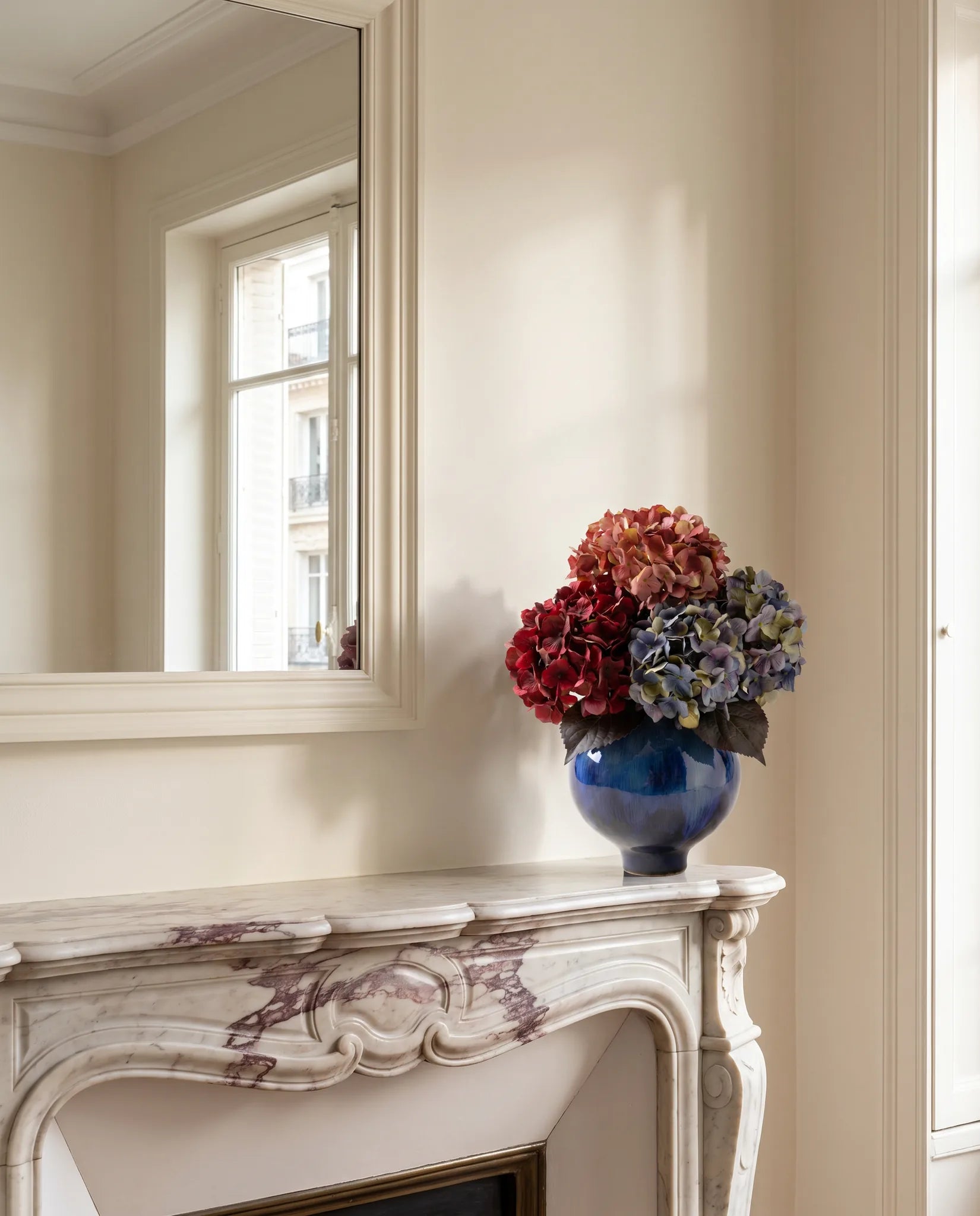 Bouquet artificiel rose et bleu sur une cheminée en marbre, devant un grand miroir