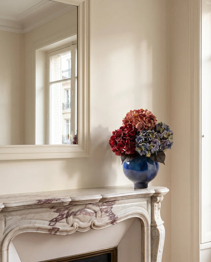Bouquet artificiel rose et bleu sur une cheminée en marbre, devant un grand miroir
