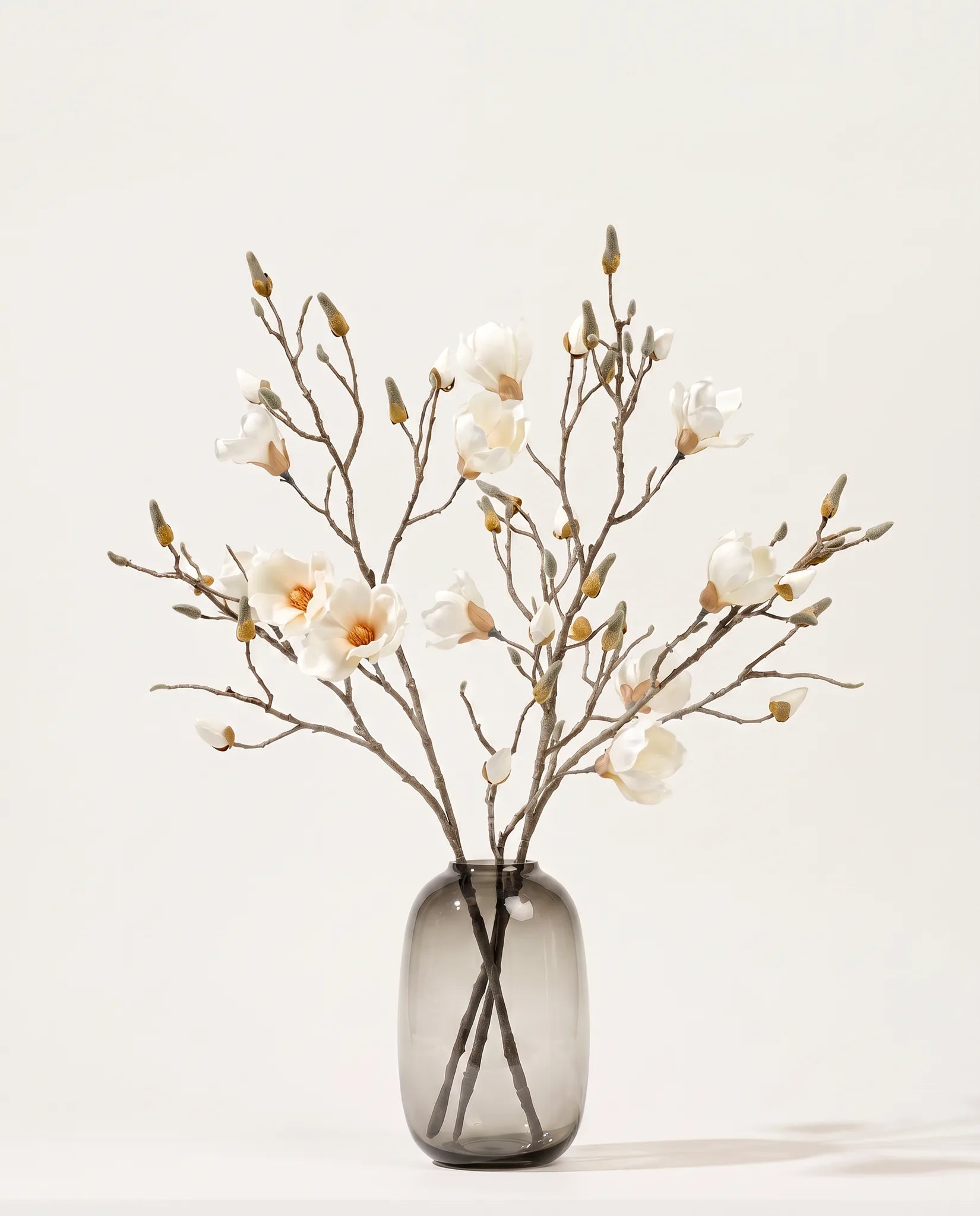 Branches de magnolia artificielles blanches dans un vase en verre ambré