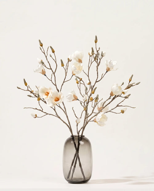 Branches de magnolia artificielles blanches dans un vase en verre ambré