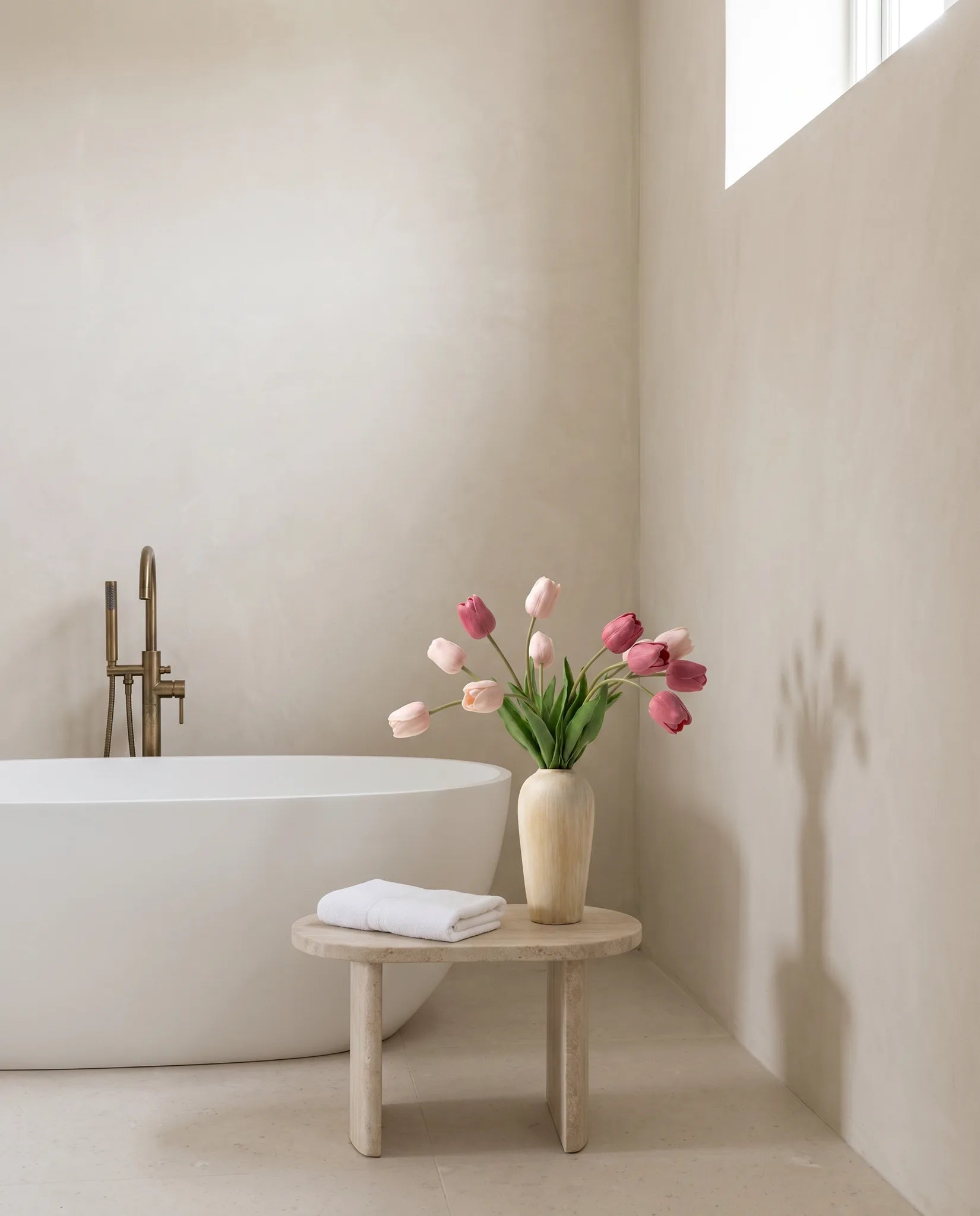 Bouquet artificiel rose sur un tabouret en pierre, près d'une baignoire îlot