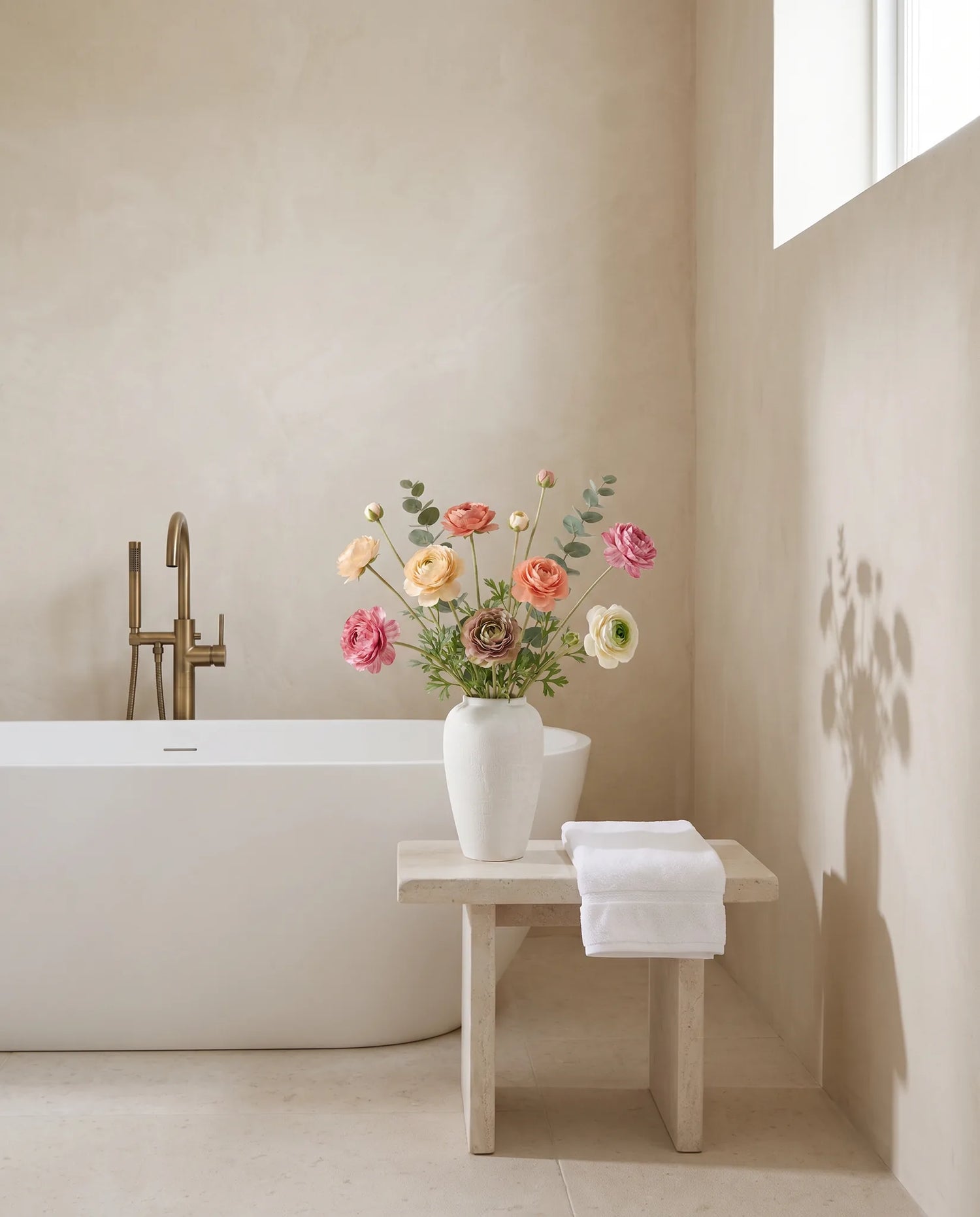 Bouquet artificiel multicolore dans une salle de bain, tabouret en pierre et baignoire îlot