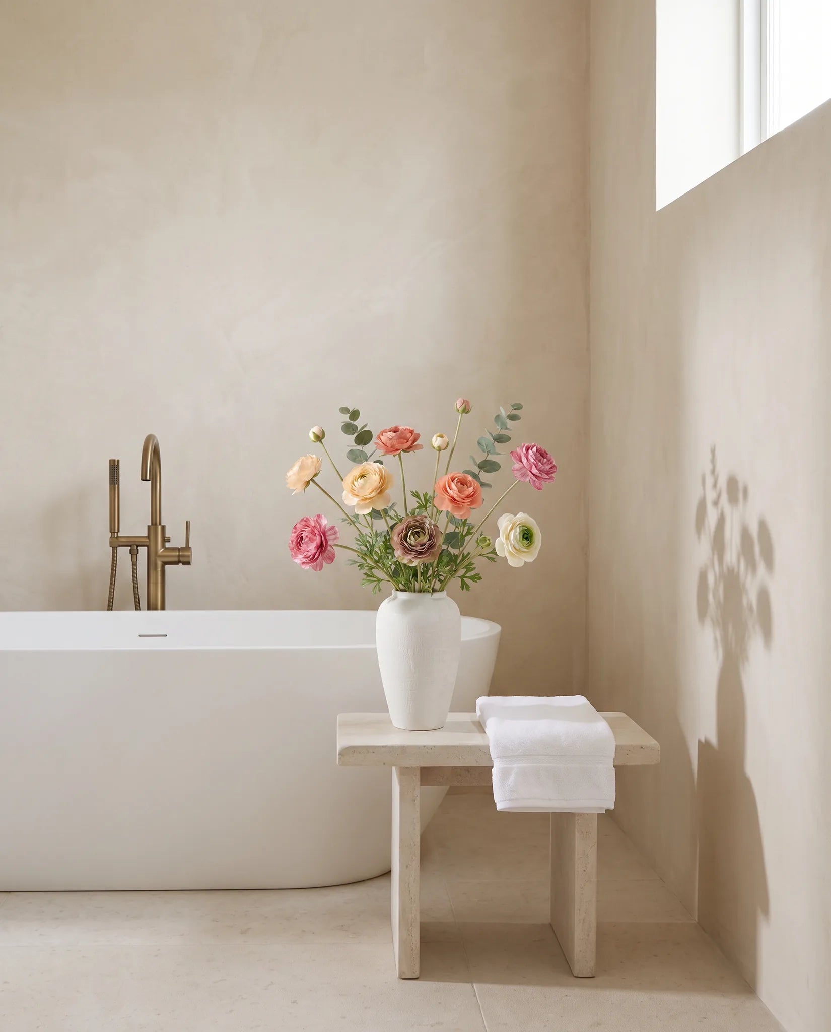 Bouquet artificiel multicolore dans une salle de bain, tabouret en pierre et baignoire îlot