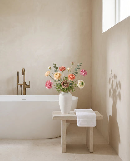 Bouquet artificiel multicolore dans une salle de bain, tabouret en pierre et baignoire îlot