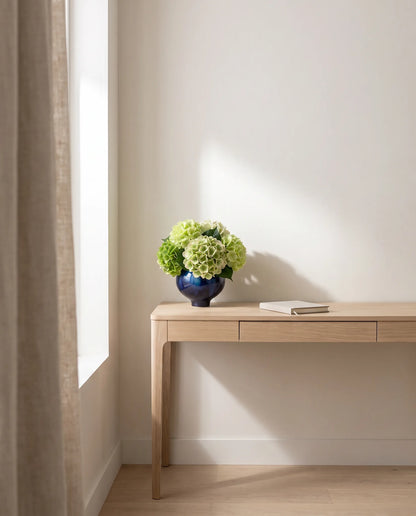 Bouquet artificiel vert d'eau sur la table en chêne clair d'un bureau au rideau en lin