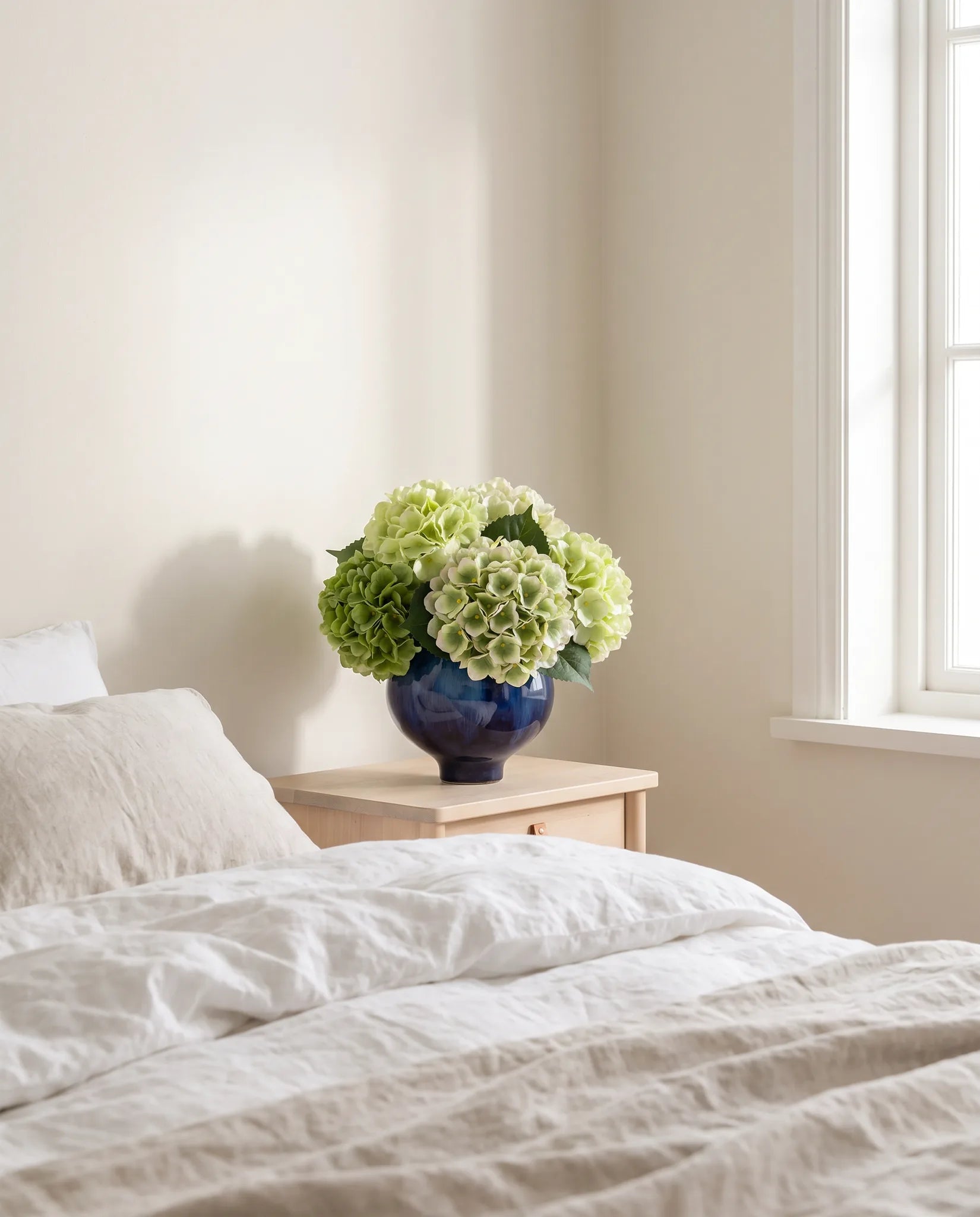 Bouquet artificiel vert d'eau sur une table de chevet, chambre au linge de lit en lin
