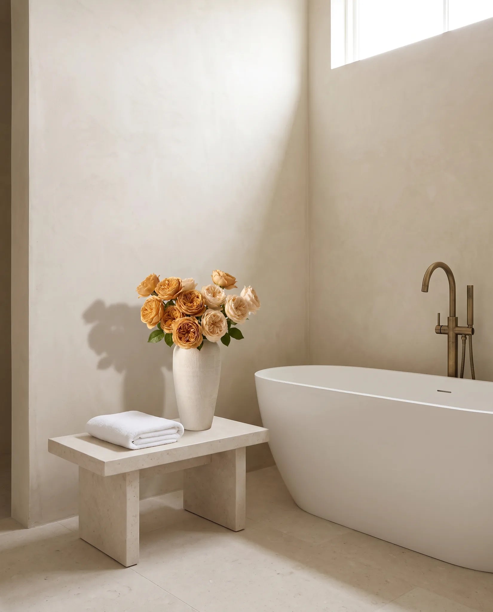 Bouquet artificiel champagne dans une salle de bain, baignoire îlot et tabouret en pierre