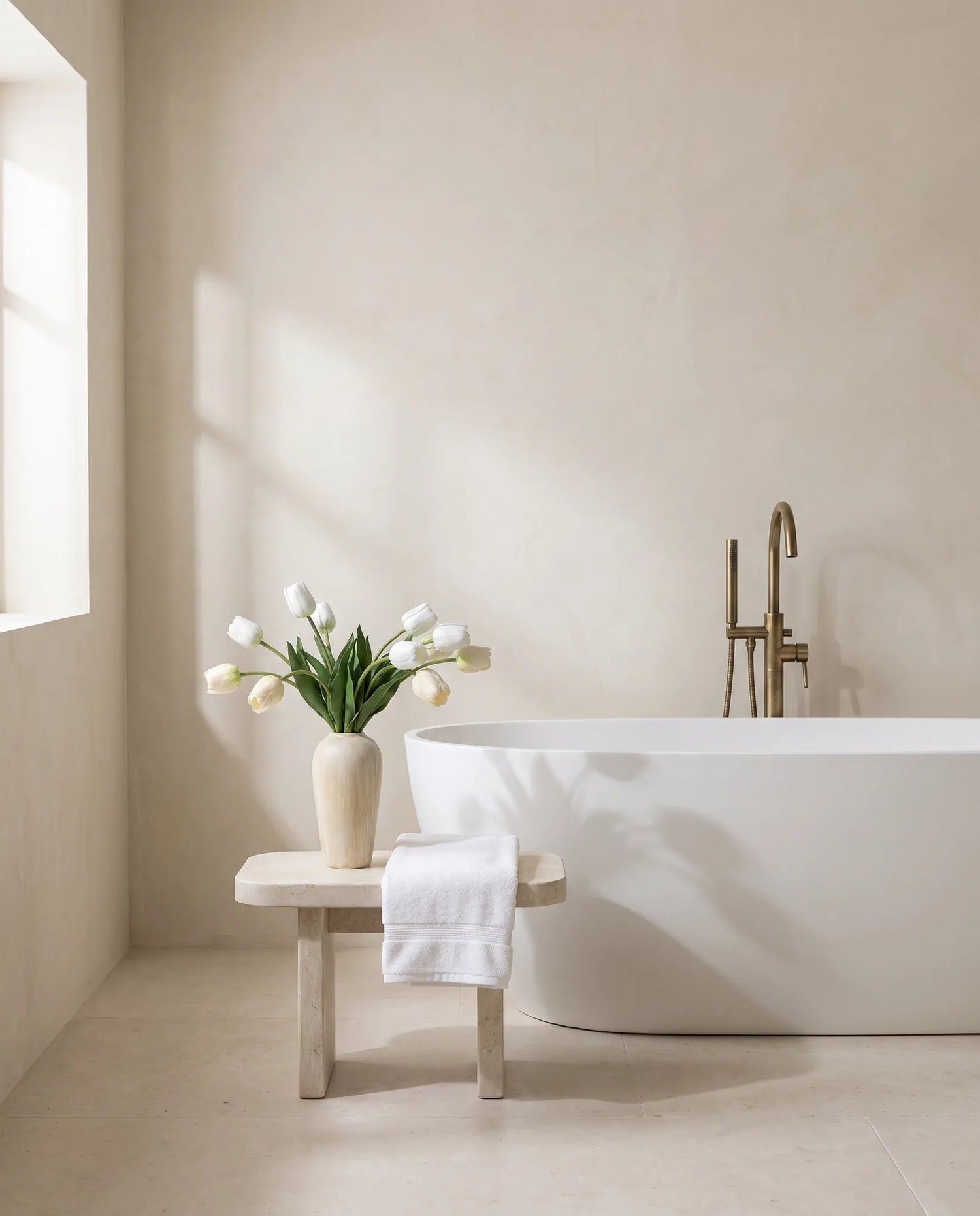 Bouquet artificiel blanc près d'une baignoire îlot, tabouret en pierre et laiton vieilli