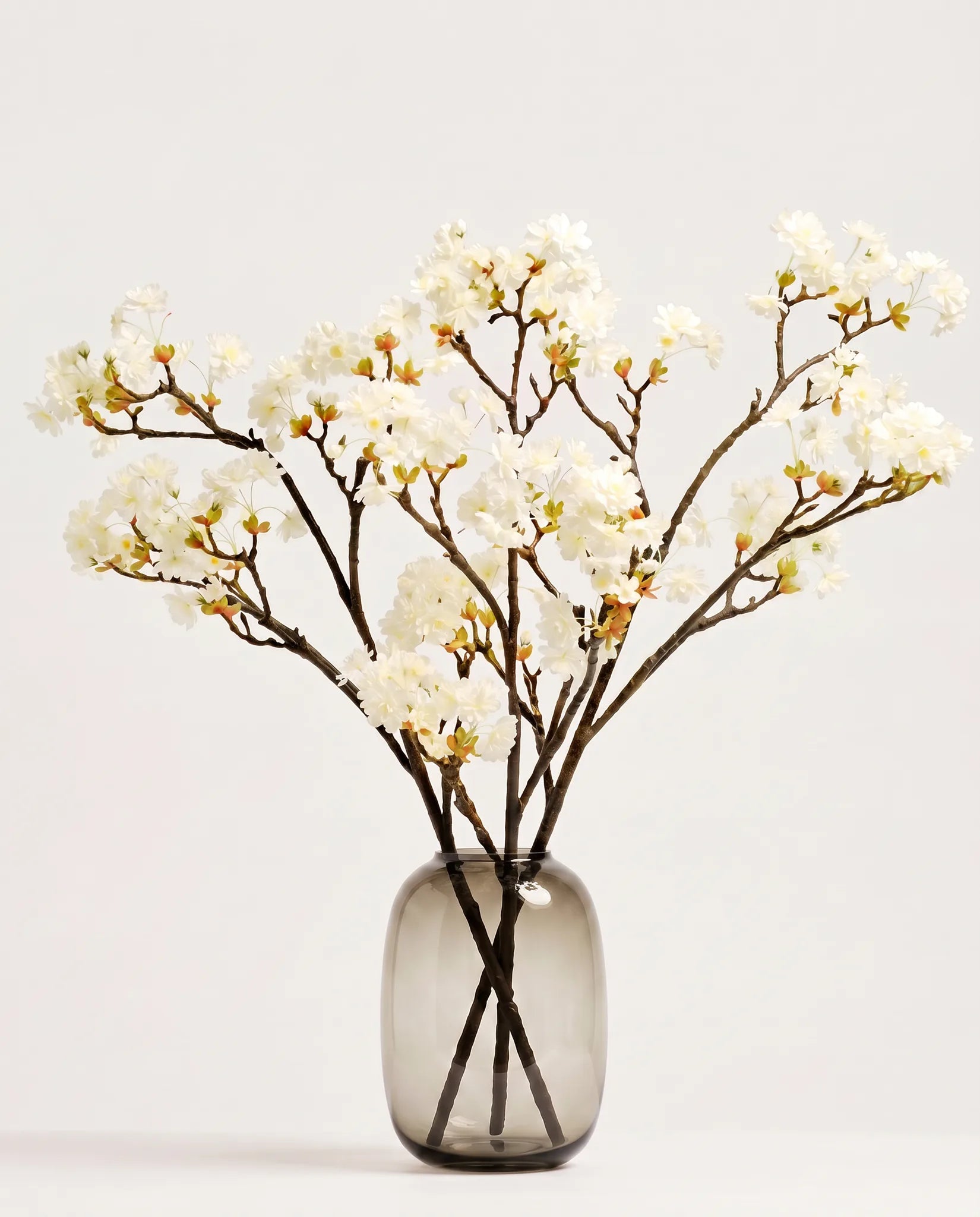 Branches de cerisier artificielles blanches dans un vase en verre ambré