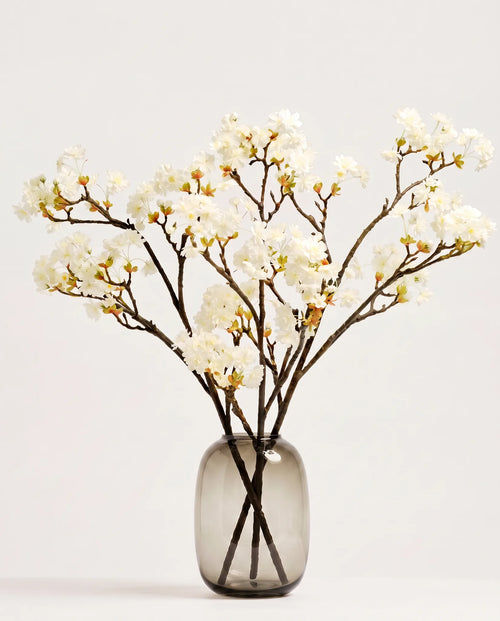 Branches de cerisier artificielles blanches dans un vase en verre ambré