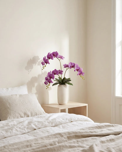 Bouquet artificiel violet sur une table de chevet en bois clair, chambre au petit matin