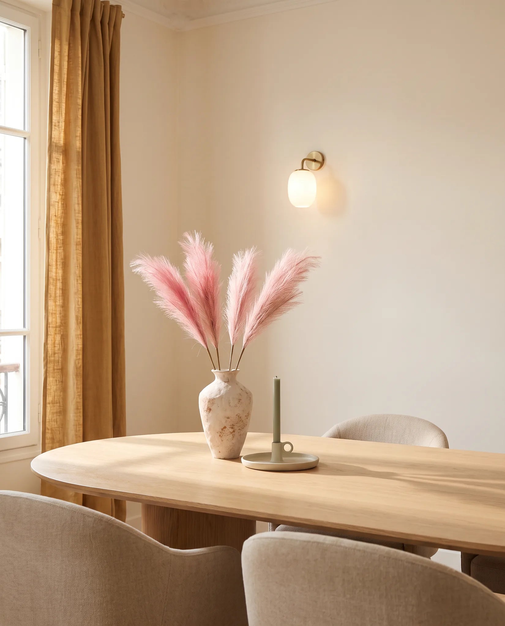Grandes graminées artificielles rose poudré dans une salle à manger, table en chêne clair