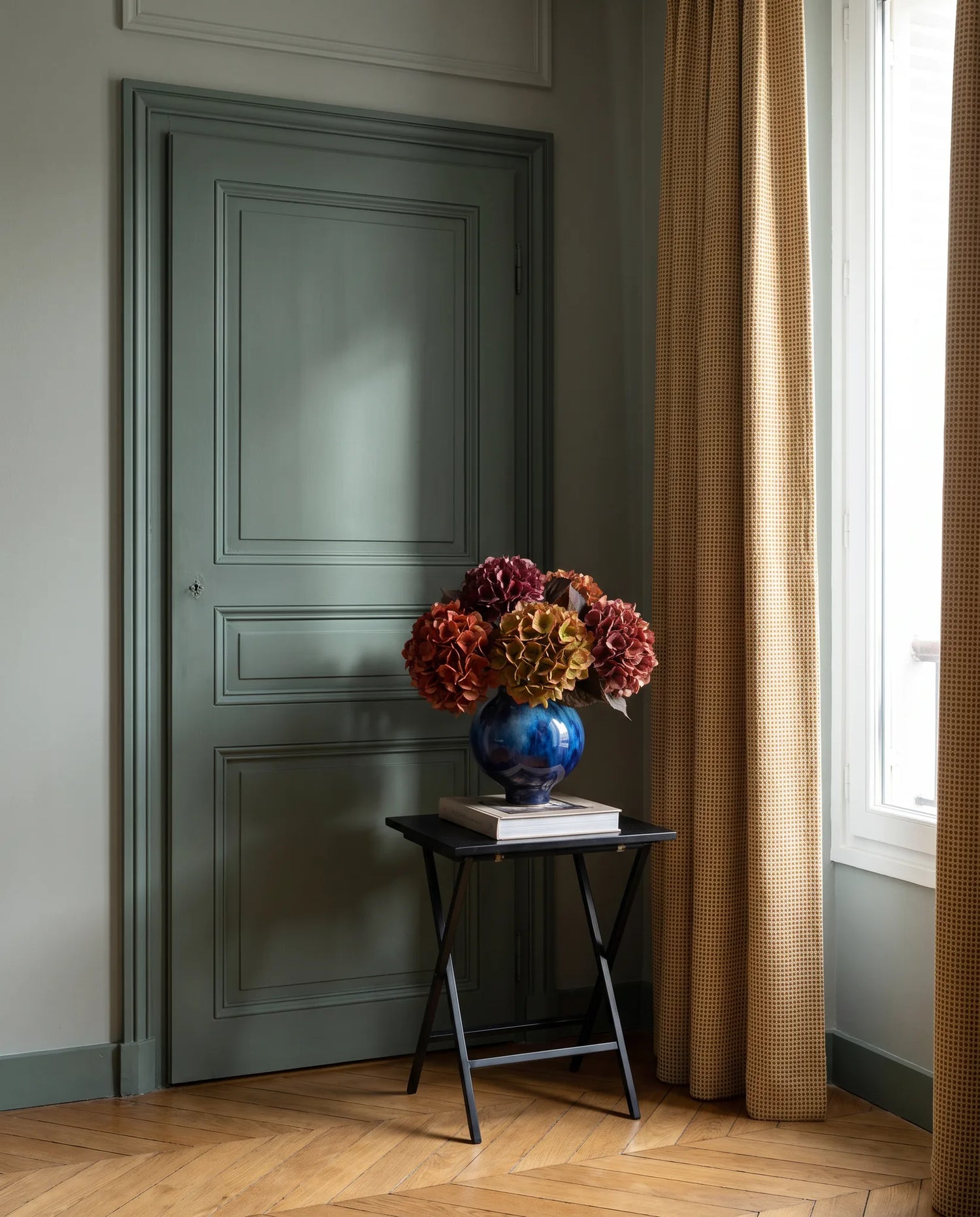 Bouquet artificiel rouge bordeaux sur une table d'appoint noire, entrée vert sauge