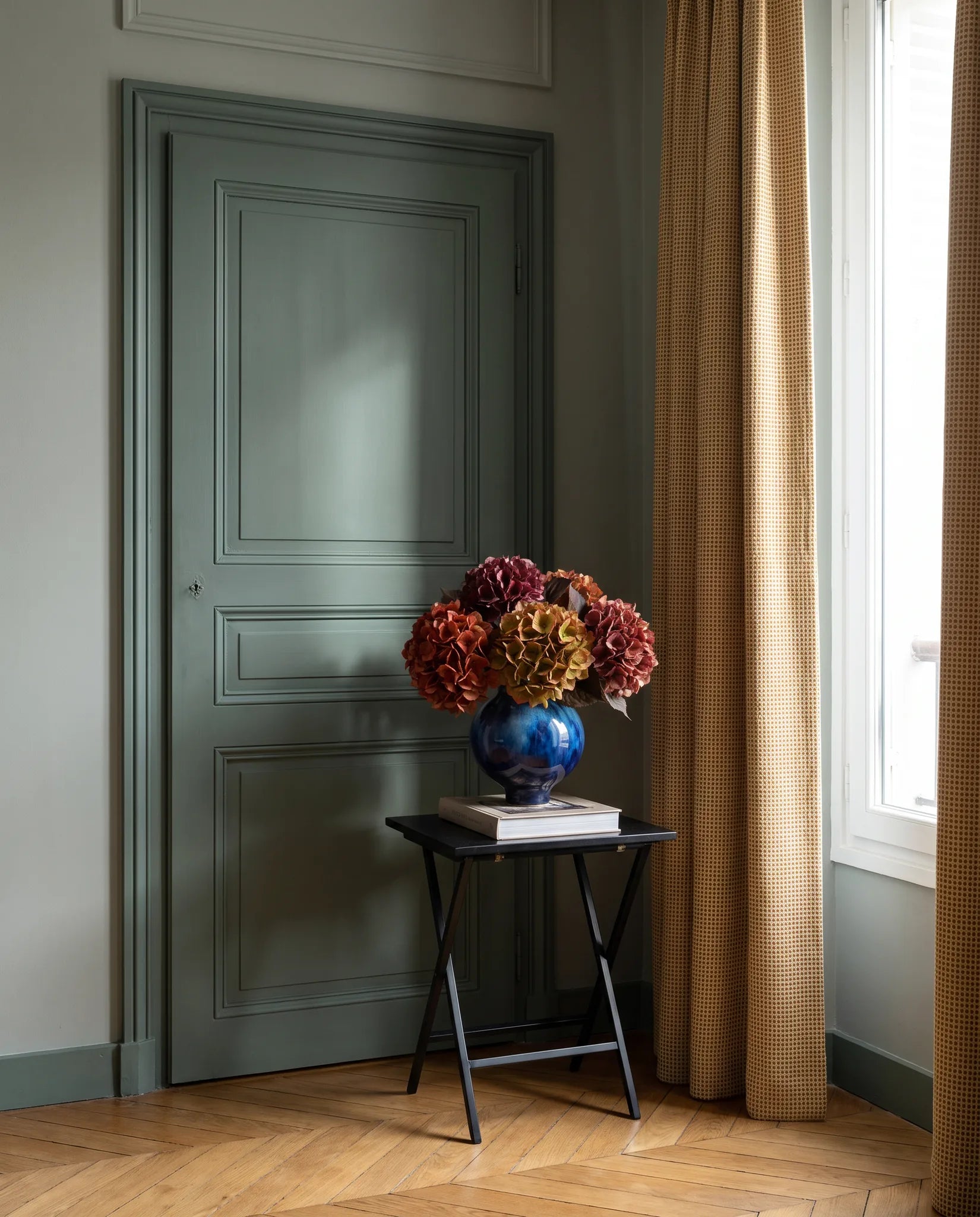 Bouquet artificiel rouge bordeaux sur une table d'appoint noire, entrée vert sauge
