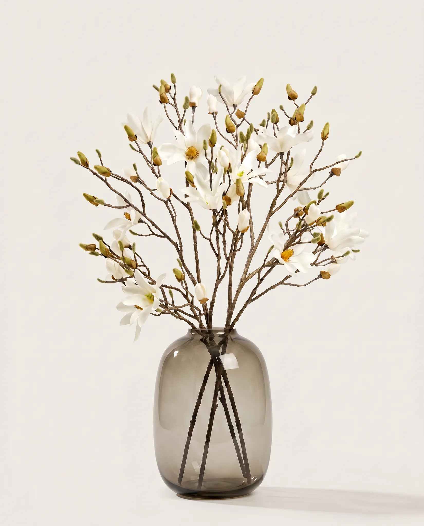 Grand bouquet artificiel de magnolias crème dans un vase en verre ambré