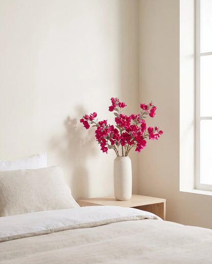 Bouquet artificiel magenta dans une chambre, table de chevet en bois clair au petit matin