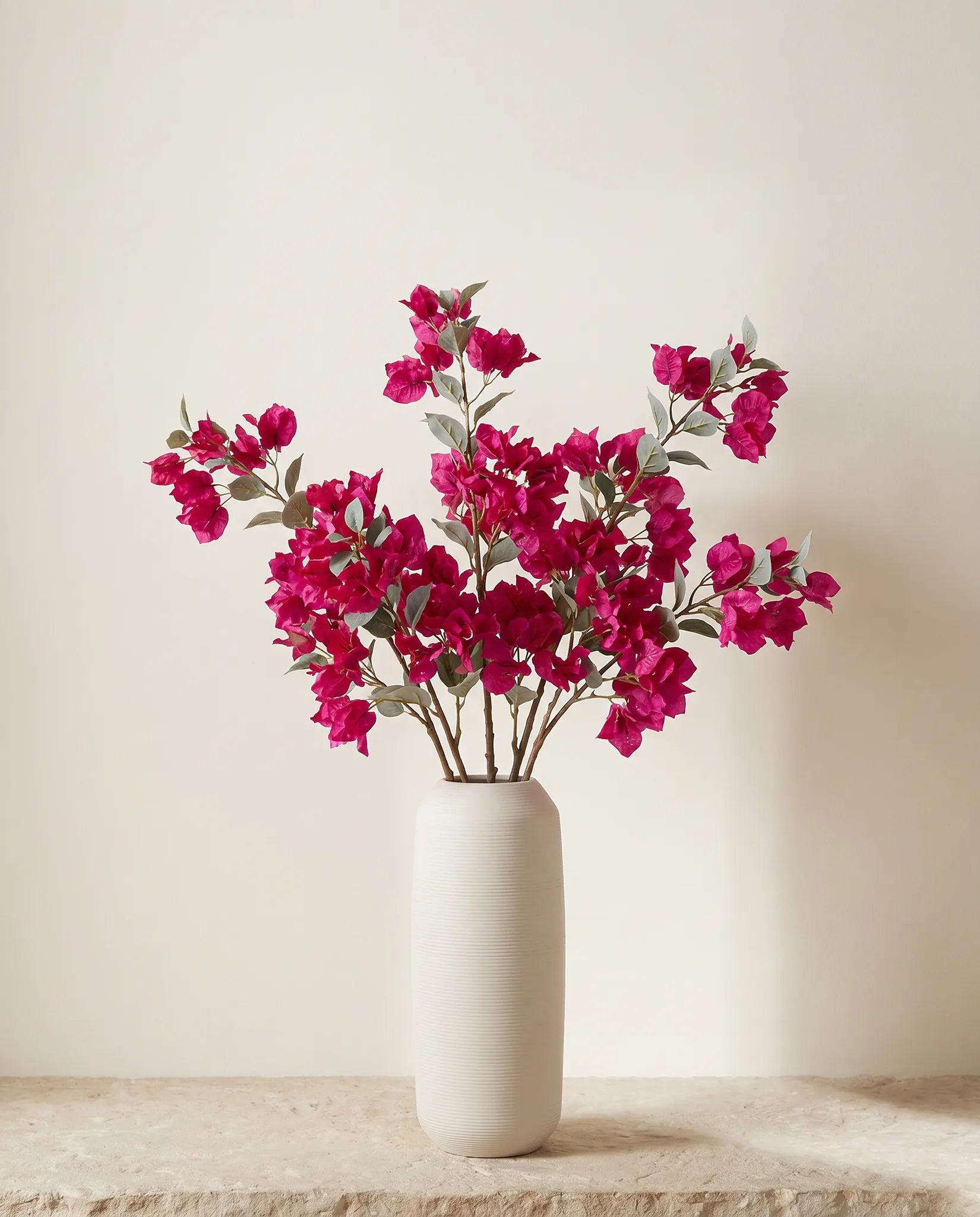 Bouquet artificiel magenta fuchsia posé sur un plan de travail en pierre claire