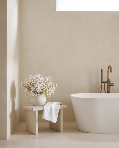 Bouquet artificiel blanc sur un tabouret en pierre près d'une baignoire îlot