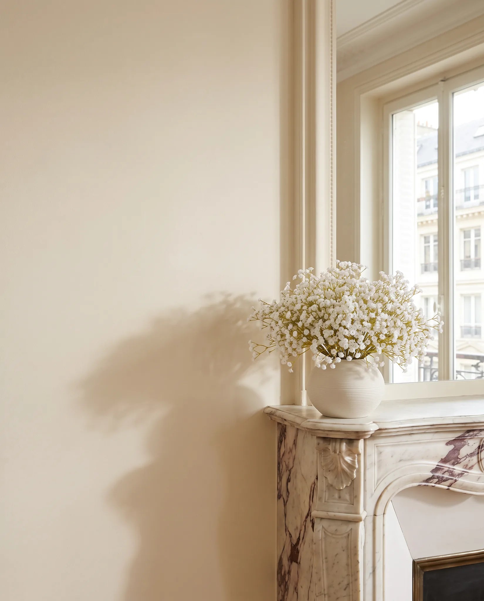 Bouquet artificiel blanc sur une cheminée en marbre, devant le miroir d'un salon