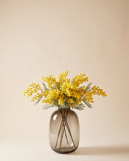 Bouquet artificiel de mimosa jaune dans un vase en verre ambré