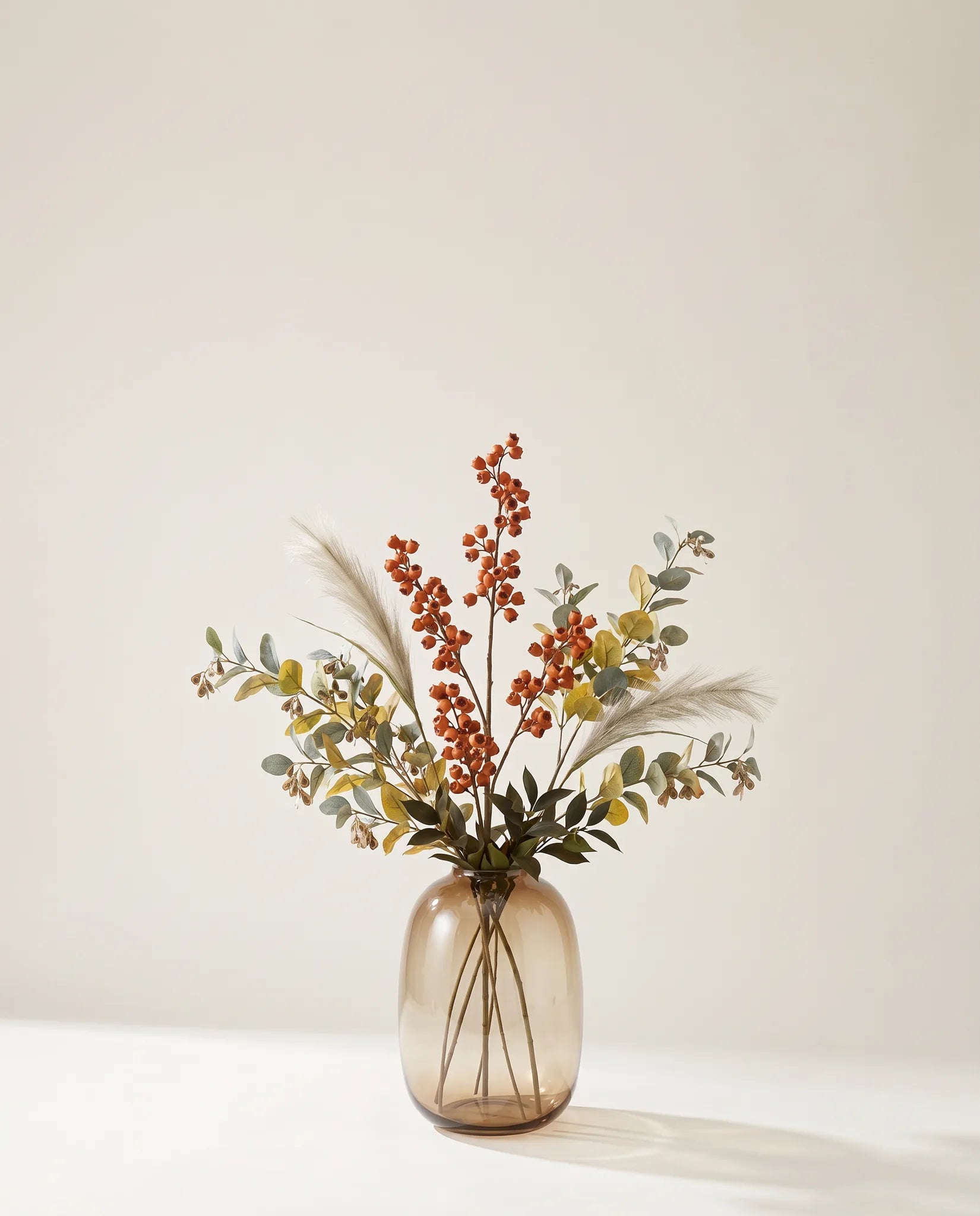 Feuillage artificiel de clochettes, eucalyptus et ruscus rouille et vert dans un vase en verre ambré