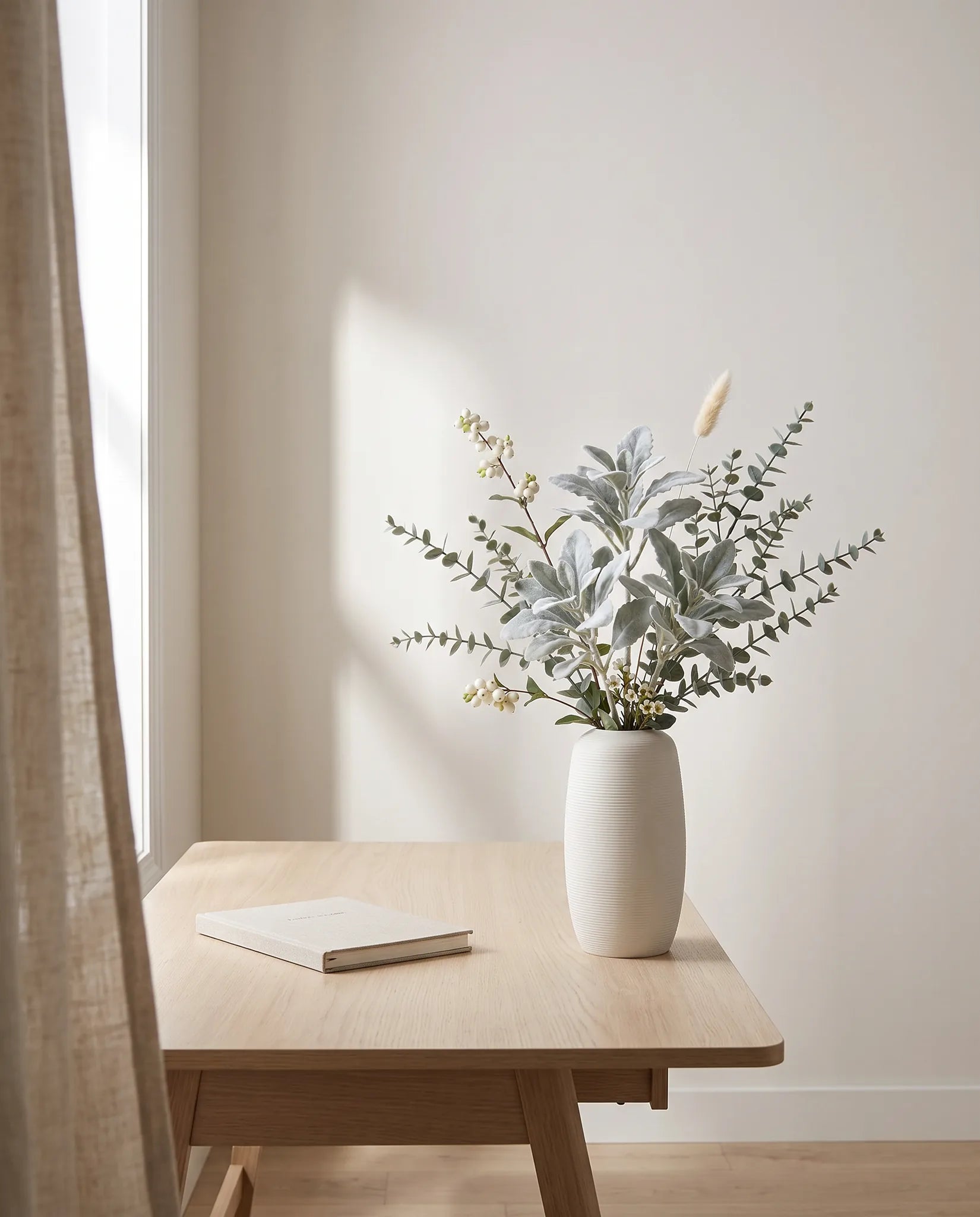 Branches artificielles argent et blanc sur une table en chêne clair dans un bureau à la lumière latérale