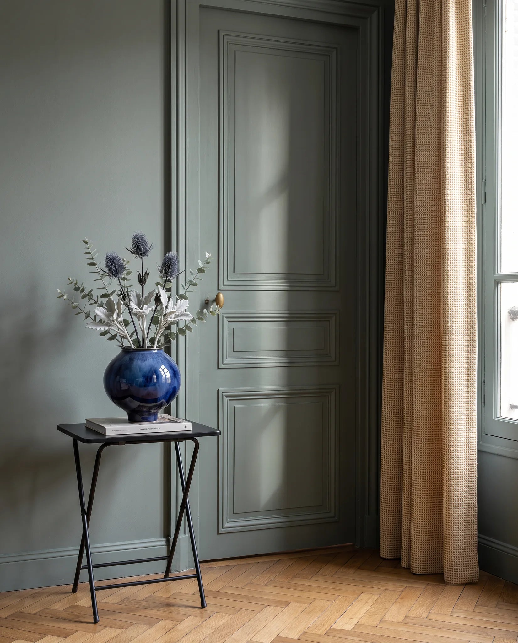 Feuillage artificiel argenté sur une table d'appoint noire dans une entrée au parquet point de Hongrie