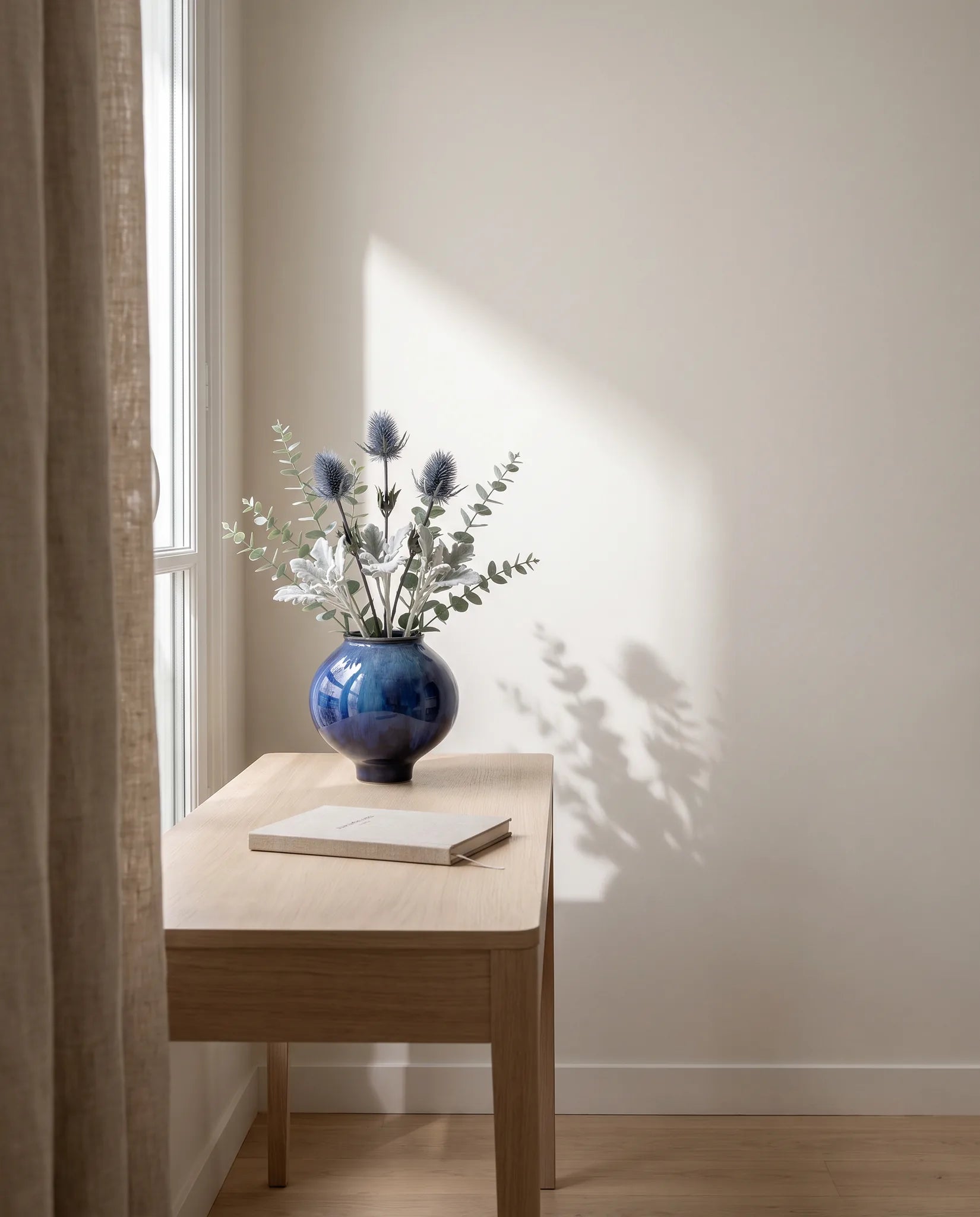 Feuillage artificiel argenté sur une table en chêne clair dans un bureau en lumière latérale