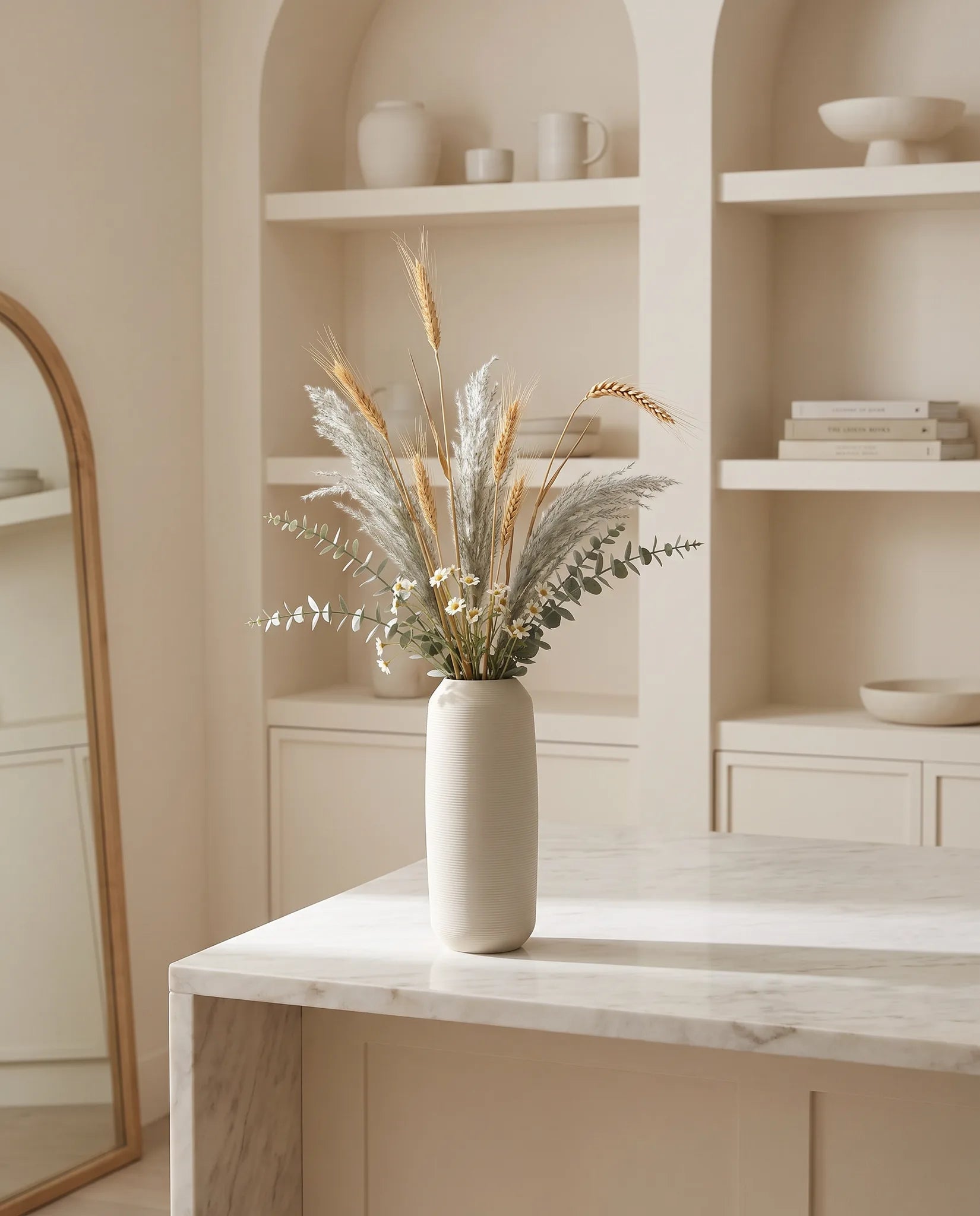 Plante artificielle dorée et vert-gris sur un îlot en marbre clair dans une cuisine crème