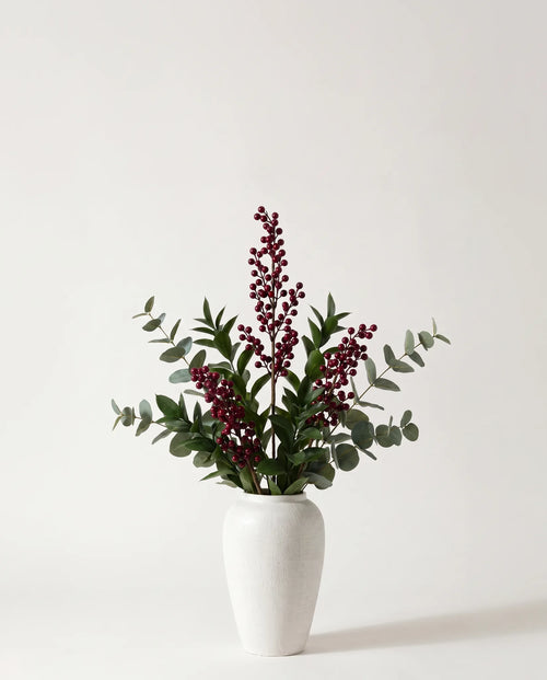 Branches artificielles de baies, ruscus et eucalyptus vert-foncé et bordeaux dans un vase en céramique