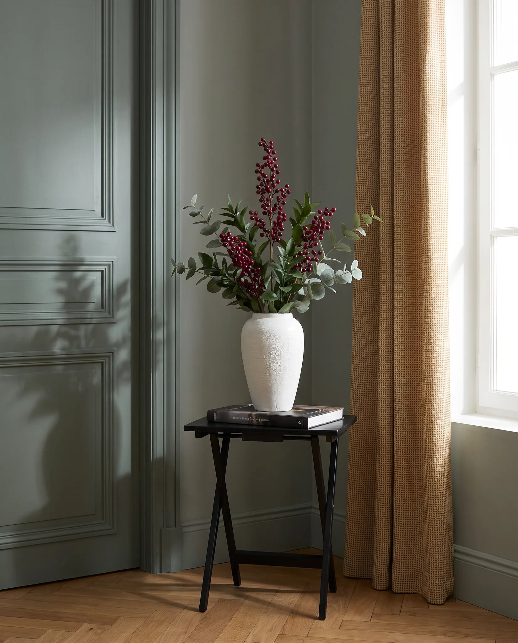 Branches artificielles vert-foncé et bordeaux sur une table d'appoint noire dans une entrée au parquet point de Hongrie
