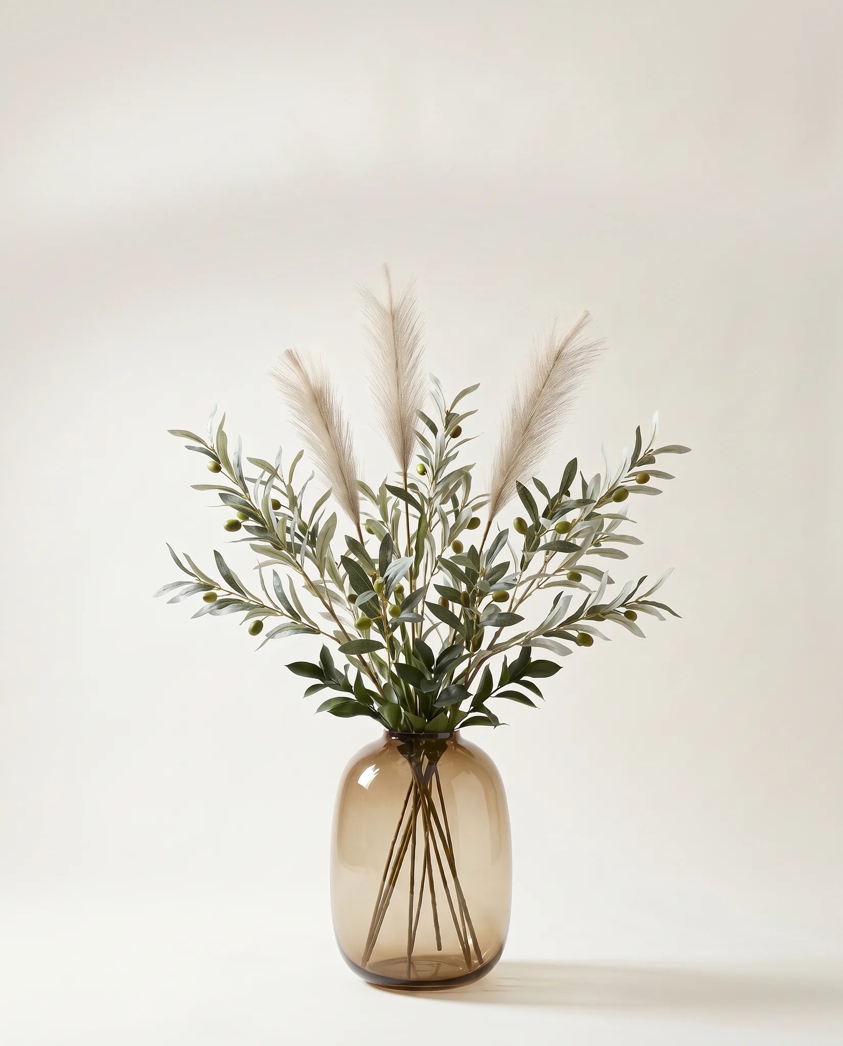 Branches artificielles d'olivier et ruscus vert-olive et crème dans un vase en verre ambré