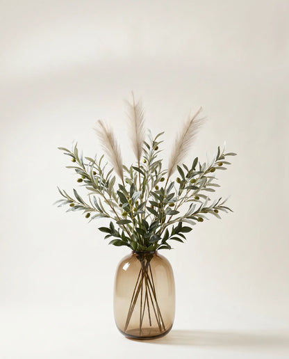 Branches artificielles d'olivier et ruscus vert-olive et crème dans un vase en verre ambré
