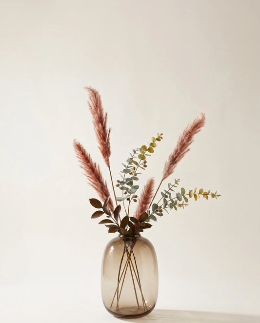 Plante artificielle d'eucalyptus, ruscus et pennisetum rose-rouille et vert dans un vase en verre ambré