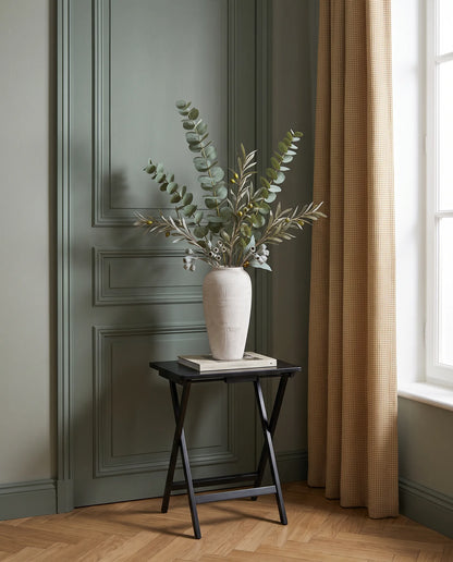 Branches artificielles vertes sur une table d'appoint noire dans une entrée au parquet point de Hongrie