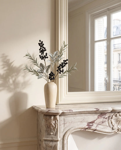 Feuillage artificiel vert argenté et noir sur une cheminée en marbre devant un grand miroir dans un salon parisien rénové